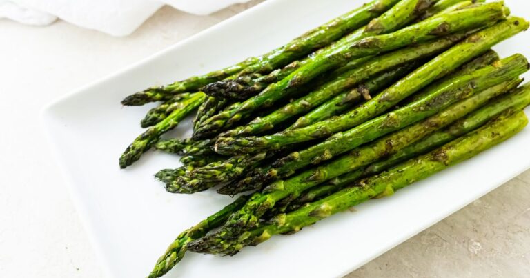 A white rectangular plate with a serving of roasted asparagus spears, lightly seasoned and arranged in a neat pile.