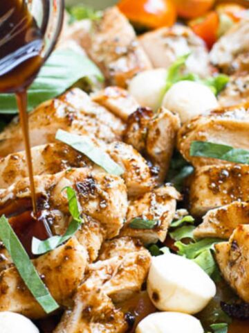Grilled chicken slices topped with fresh basil, mozzarella balls, and tomatoes are drizzled with balsamic glaze.