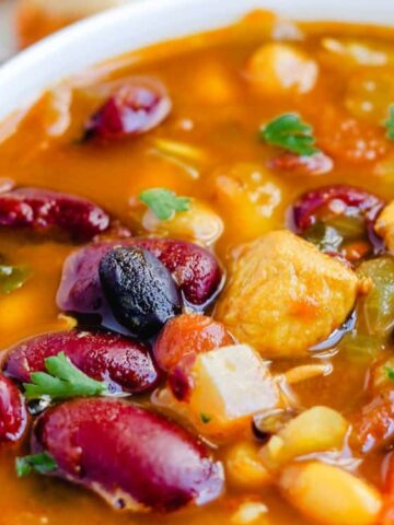 A close-up of a bowl of chili with kidney beans, black beans, corn, tomato chunks, green peppers, and garnished with parsley.