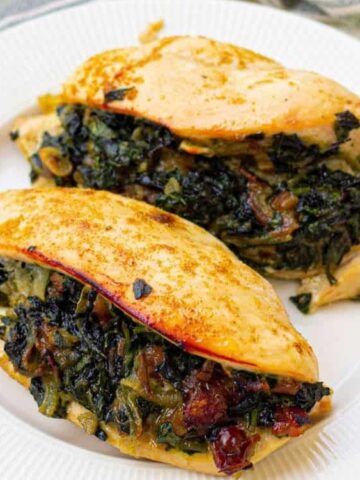 Two cooked chicken breasts stuffed with a spinach and onion mixture are served on a white plate.