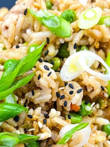 Close-up of fried rice with peas, carrots, green onions, and black sesame seeds on a dark plate.