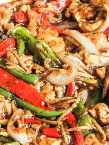 A stir-fry dish with sliced chicken, red and green bell peppers, onions, and a glossy brown sauce.