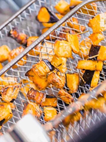 Close-up of roasted cubed vegetables, possibly potatoes or sweet potatoes, in a metal air fryer basket.