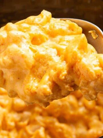 A spoonful of creamy macaroni and cheese being held above a pot filled with more macaroni and cheese.