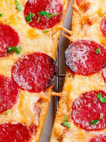 Two slices of French bread pizza topped with melted cheese, pepperoni, grated cheese, and chopped parsley on a wire rack.