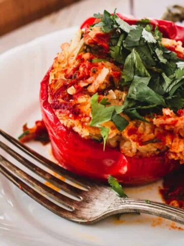 A stuffed red bell pepper filled with rice and vegetables, topped with chopped fresh herbs, is served on a white plate with a fork.