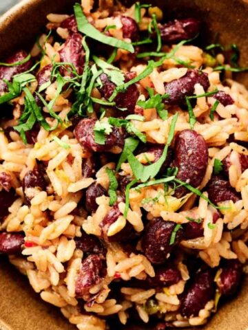 A bowl of rice and kidney beans garnished with chopped fresh herbs, served in a brown dish on a light surface.