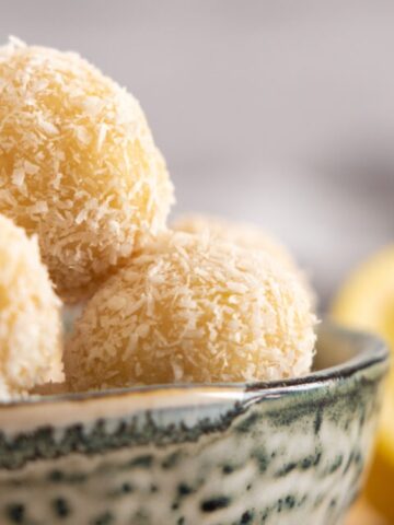 A bowl filled with round, coconut-covered dessert balls, with a sliced lemon visible in the background.