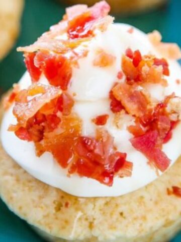 A vanilla cupcake topped with white frosting and crumbled bacon pieces, placed on a blue plate.