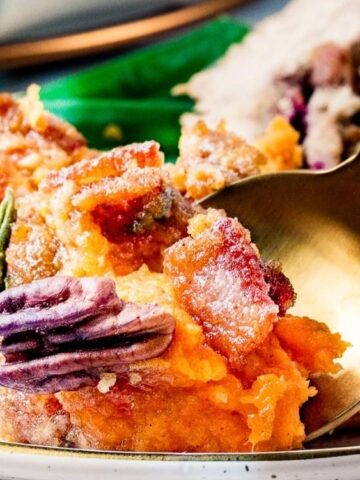 A close-up of a plate with sweet potato casserole topped with pecans, being served with a golden spoon.