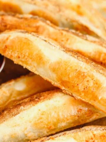 Close-up of crispy potato wedges on a tray with a side of ketchup and a side of sour cream.