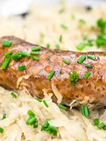 A cooked sausage topped with chopped chives rests on a bed of sauerkraut.
