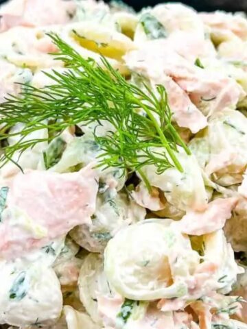 A bowl of creamy pasta salad with pieces of smoked salmon and fresh dill garnish on top.
