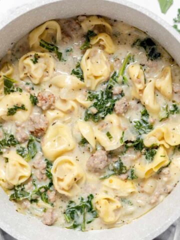 A pot filled with creamy tortellini soup containing sausage and chopped kale, viewed from above.