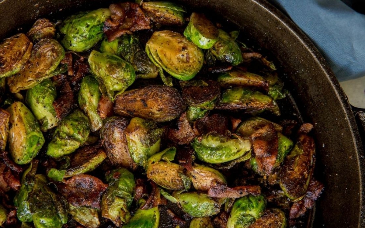 Roasted Brussels sprouts and pieces of crispy bacon are shown in a cast iron skillet.