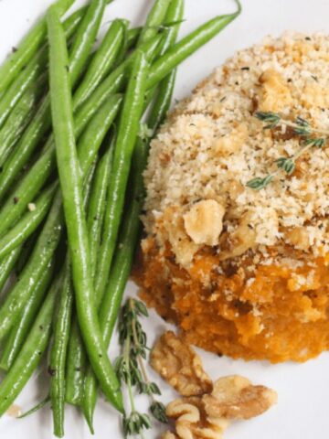 A plate with sautéed green beans and a serving of baked sweet potato casserole topped with breadcrumbs and walnuts.