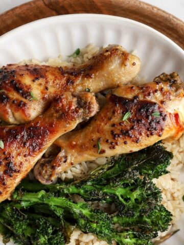 Three seasoned roasted chicken drumsticks served over rice with broccolini on a white plate, viewed from above.