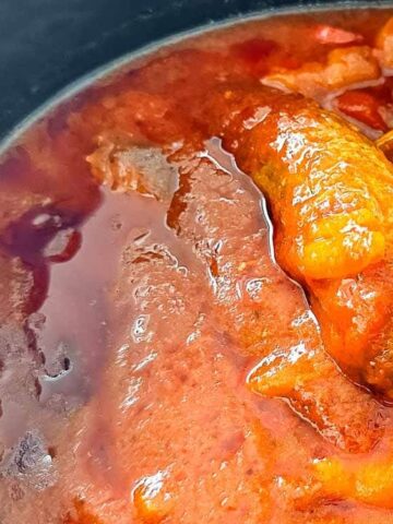 sausage and peppers on a slow cooker with wooden spoon