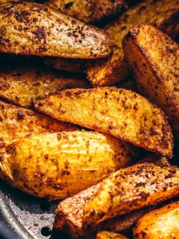 Seasoned potato wedges are arranged in an air fryer basket, showing a crispy, golden-brown exterior.