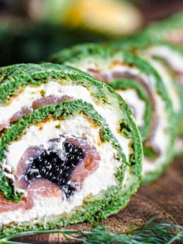 A close-up of sliced spinach and cream cheese roulades with smoked salmon and black caviar, arranged on a wooden board.