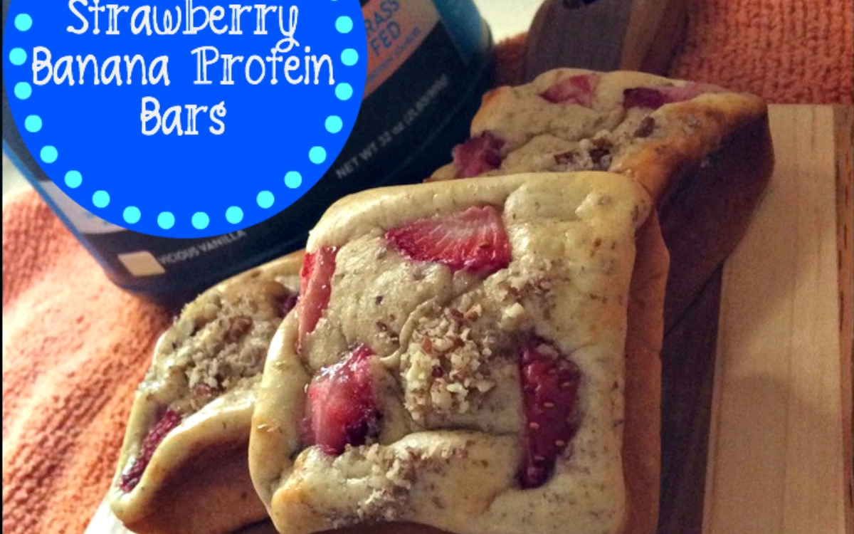 Three rectangular strawberry banana protein bars with visible strawberry slices are displayed on a wooden board, with a container of protein powder in the background. Text overlay reads: "Strawberry Banana Protein Bars.