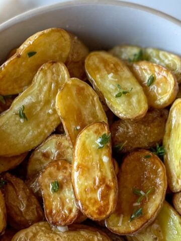A white bowl filled with roasted fingerling potatoes garnished with fresh herbs.