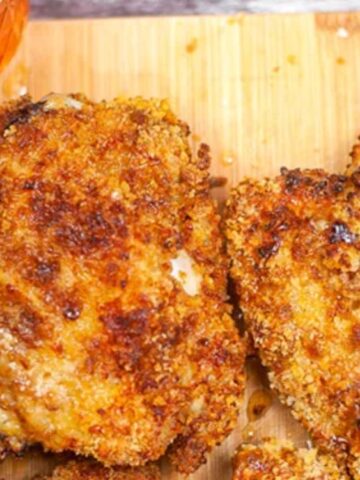 Two pieces of crispy fried chicken on a wooden cutting board, with a small jar of honey nearby.