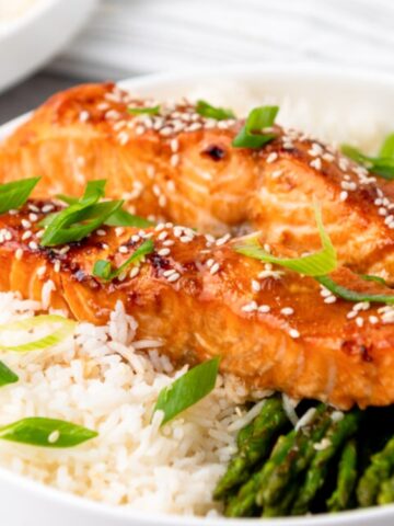 A plate with rice, grilled salmon topped with sesame seeds and green onions, and a side of asparagus.