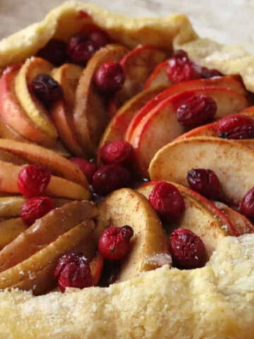A rustic galette with a flaky crust, filled with sliced apples, pears, and whole cranberries, arranged in a circular pattern.