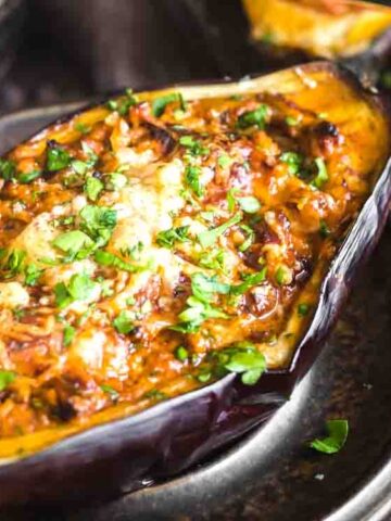 Roasted eggplant half filled with a savory, cheesy tomato and herb mixture, garnished with chopped fresh parsley, served on a dark plate.