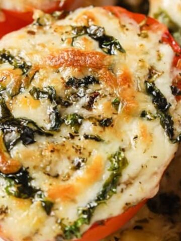 Baked tomato halves topped with melted cheese, chopped spinach, and herbs on a baking sheet.