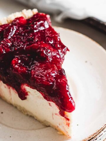 A slice of cheesecake topped with a thick layer of mixed berry sauce on a white plate.