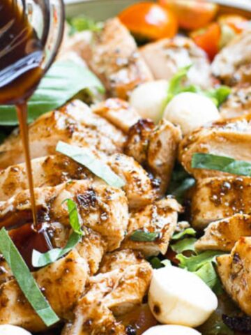 Sliced grilled chicken with fresh mozzarella, basil, tomatoes, and greens is drizzled with a dark balsamic dressing.