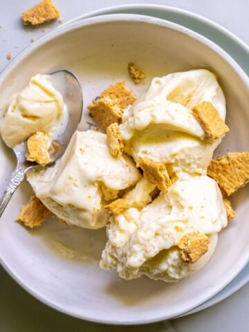 A bowl of vanilla ice cream with crumbled graham crackers on top, served with a spoon.