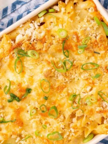 A baked casserole topped with melted cheese, breadcrumbs, and sliced green onions in a white dish, resting on a blue patterned cloth.