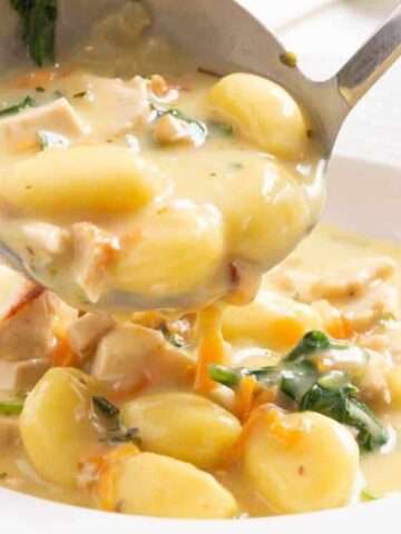 A ladle serving creamy chicken gnocchi soup with chunks of chicken, gnocchi, and spinach into a white bowl.