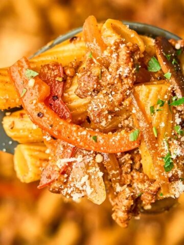 A close-up of a spoon holding pasta with ground meat, red bell peppers, tomato sauce, and sprinkled grated cheese.