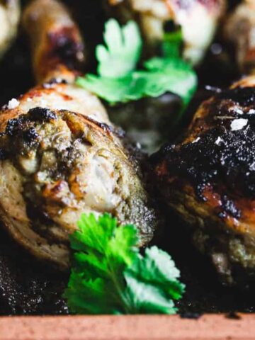 Close-up of grilled chicken drumsticks garnished with fresh cilantro and coarse salt, with a lime wedge in the background.