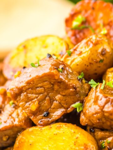 A close-up of a plate with seasoned roasted potatoes and seared beef cubes, garnished with chopped herbs.