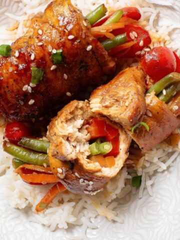 A plate of white rice topped with stuffed chicken breasts, green beans, cherry tomatoes, and carrots, garnished with green onions and sesame seeds.