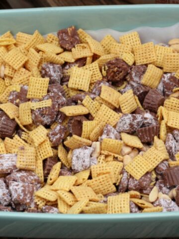 A baking dish filled with Chex cereal, peanuts, mini peanut butter cups, and chocolate-covered snack pieces coated in powdered sugar.