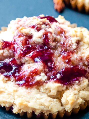 A close-up of a muffin in a paper liner topped with a swirl of fruit jam, set on a dark surface.