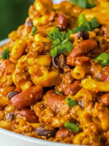 Close-up of a bowl filled with chili mac featuring macaroni noodles, kidney beans, ground meat, sauce, and topped with chopped green onions.