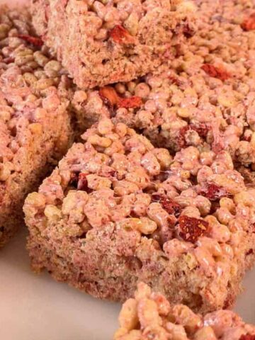 Rectangular strawberry rice crispy treats arranged in a white dish, showing crispy cereal pieces and bits of dried strawberries.