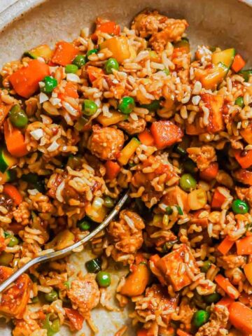 A bowl of vegetable fried rice with peas, carrots, and tofu pieces, served with a fork.