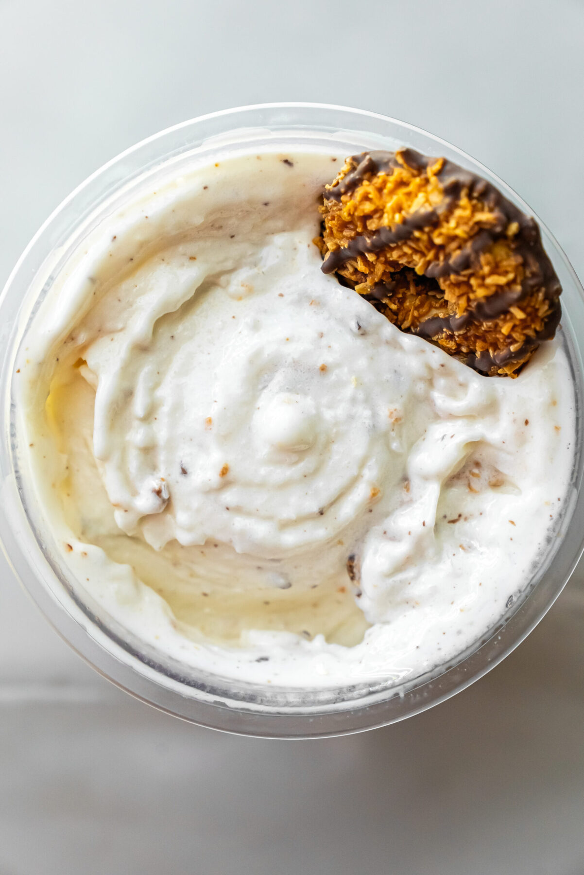 Overhead view of creamy white Caramel DeLites Ninja Creami Ice Cream in a clear pint, swirled with caramel bits and topped with a Girl Scout Caramel DeLite cookie.