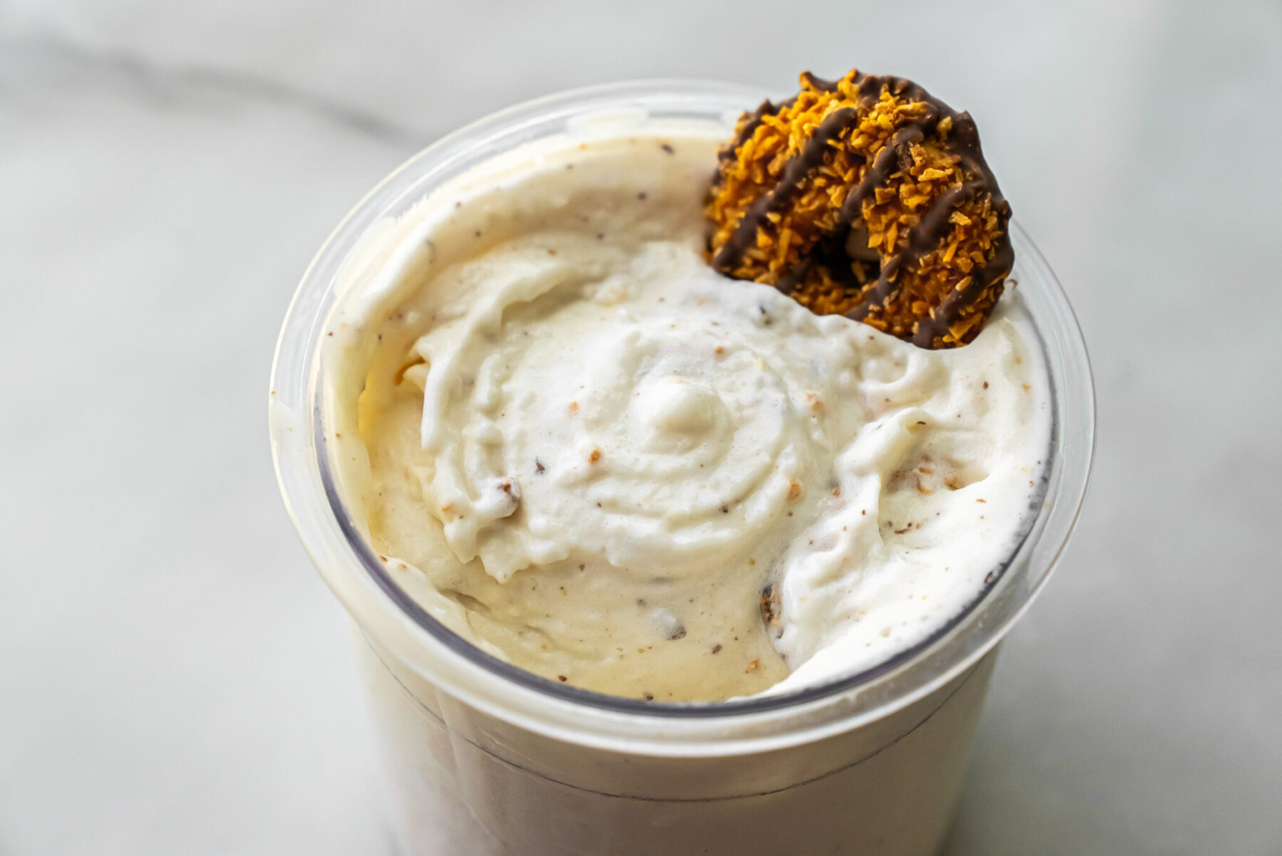 Slightly angled close-up of Caramel DeLites Ninja Creami Ice Cream in pint, swirls visible, topped with a broken Caramel DeLite cookie showing toasted coconut and chocolate drizzle.