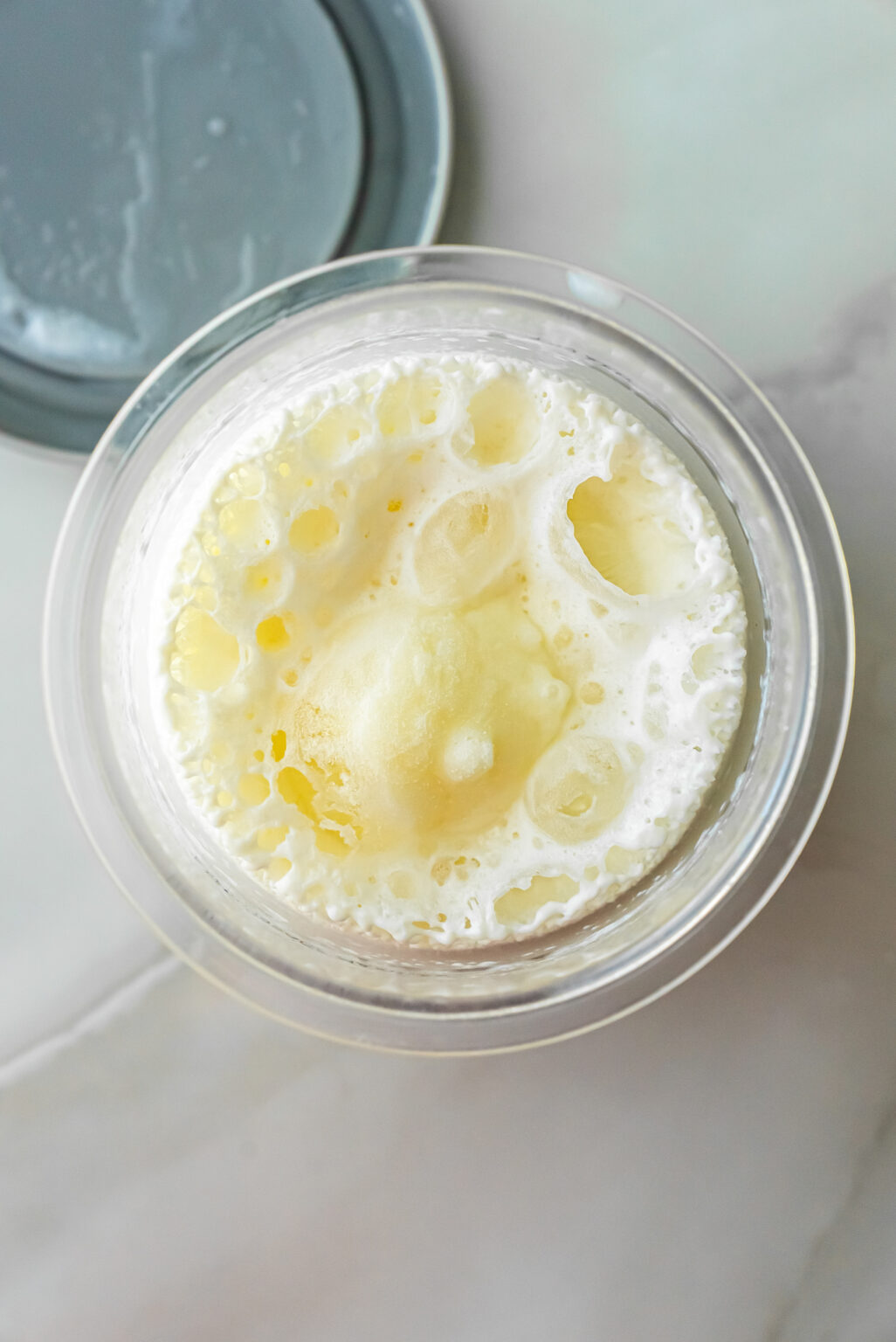 Overhead shot of a frothy, pale yellow liquid base inside a clear Ninja Creami pint, ready to be frozen before processing into Caramel DeLites Ninja Creami Ice Cream.