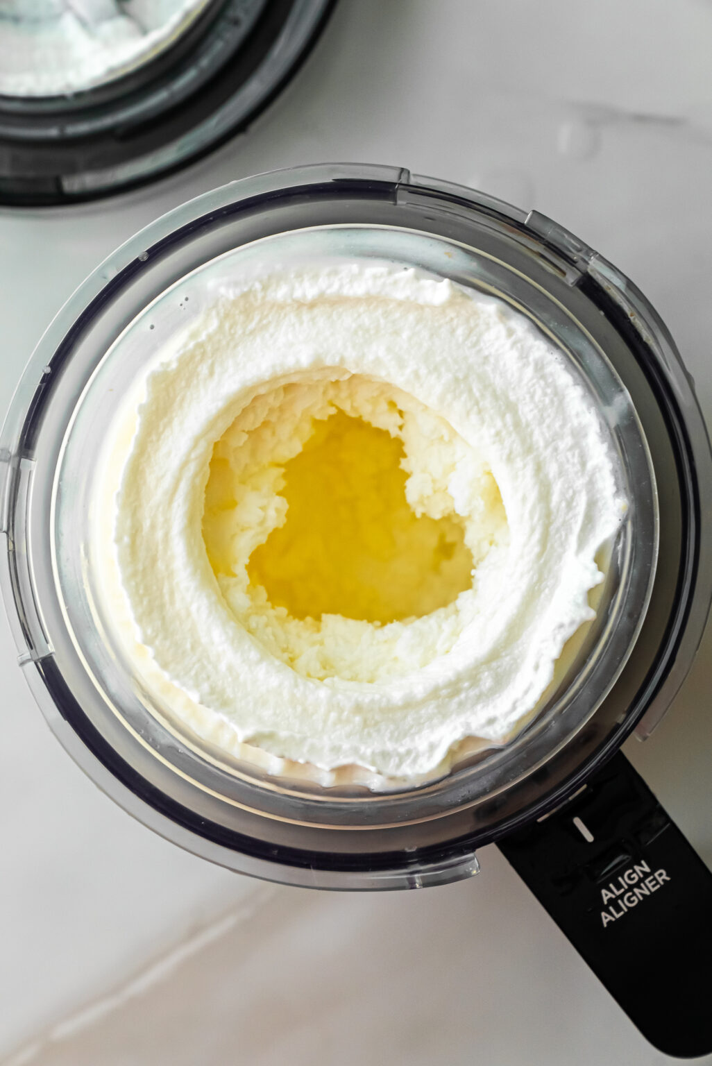 Top-down view of churned white ice cream in a Ninja Creami pint with a hollow center, showing the texture after the initial spin cycle for Caramel DeLites Ninja Creami Ice Cream.
