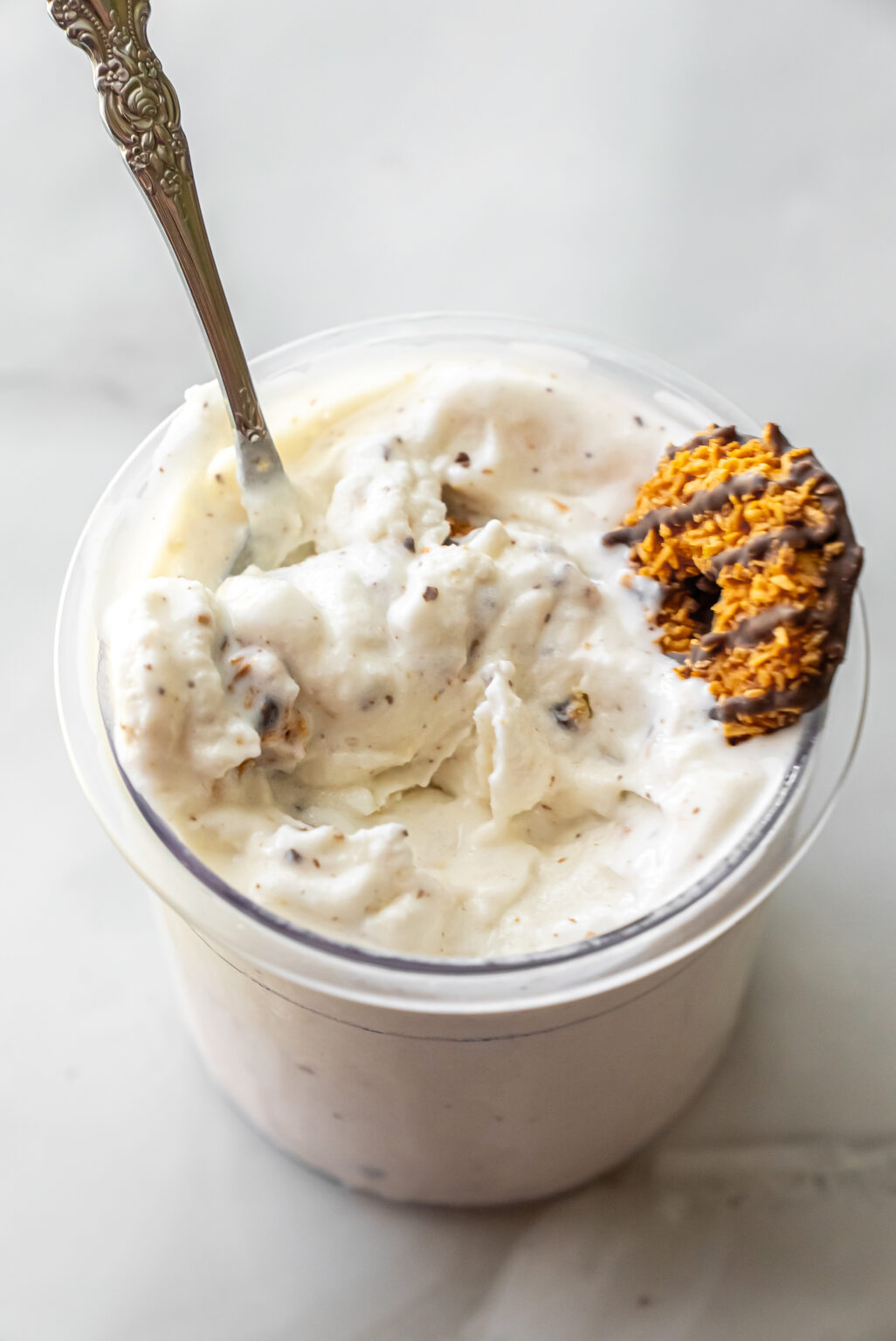 Close-up of finished Caramel DeLites Ninja Creami Ice Cream in a pint with an ornate silver spoon inserted. A half-eaten cookie garnishes the rim, showing mixed cookie bits throughout.